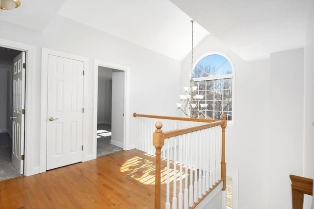 hall with wood finished floors, an upstairs landing, lofted ceiling, and a chandelier