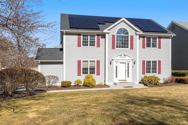 colonial inspired home with roof with shingles, solar panels, and a front lawn