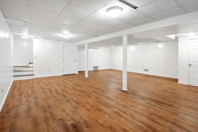 finished below grade area featuring visible vents, baseboards, stairway, wood finished floors, and a paneled ceiling