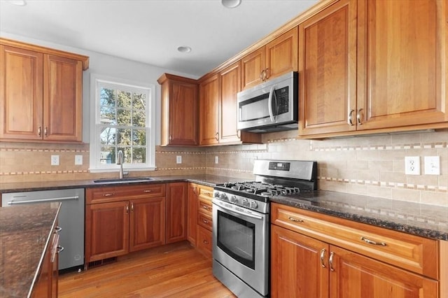 kitchen with a sink, brown cabinets, appliances with stainless steel finishes, and light wood-style flooring