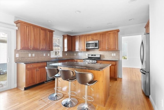 kitchen with a kitchen island, brown cabinets, appliances with stainless steel finishes, light wood-style floors, and a sink