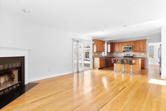 living room featuring a fireplace with flush hearth, baseboards, and light wood finished floors