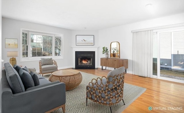 living area with baseboards, a lit fireplace, and wood finished floors