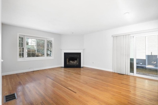 unfurnished living room with visible vents, baseboards, a fireplace with flush hearth, and wood finished floors