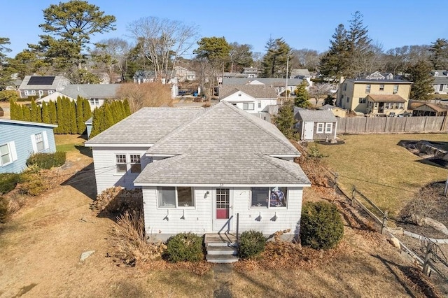 view of front of property featuring a front yard, fence, a residential view, and roof with shingles