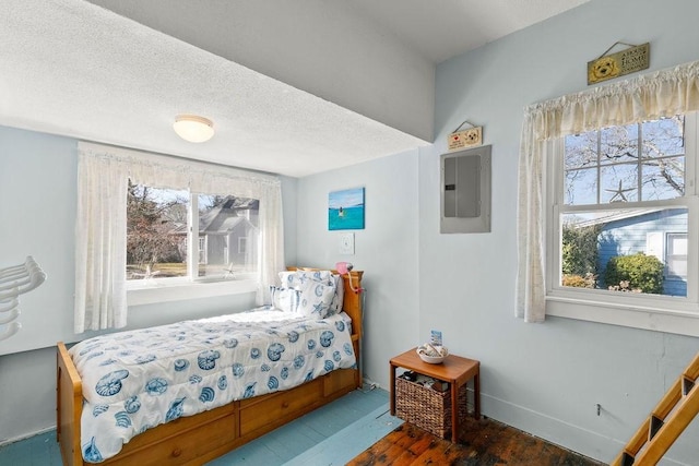 bedroom with multiple windows, electric panel, wood finished floors, and a textured ceiling