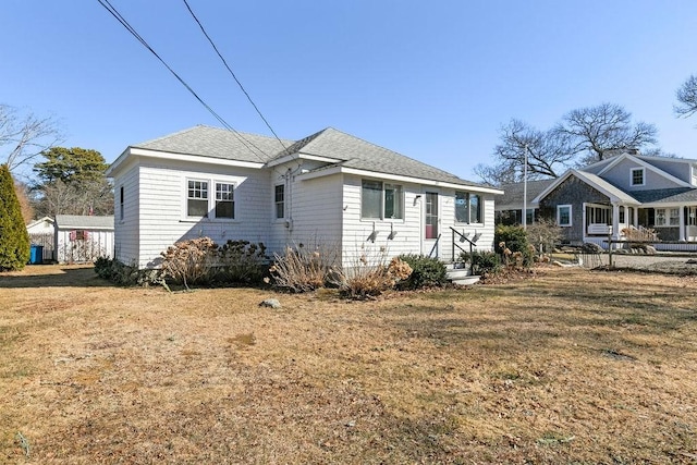 rear view of house with a lawn, a shingled roof, and entry steps