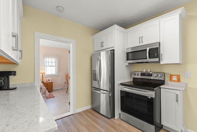 kitchen featuring light wood-style flooring, white cabinetry, stainless steel appliances, and baseboards