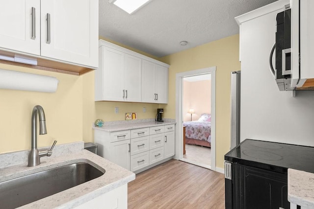 kitchen featuring light stone counters, light wood finished floors, a sink, a textured ceiling, and white cabinetry