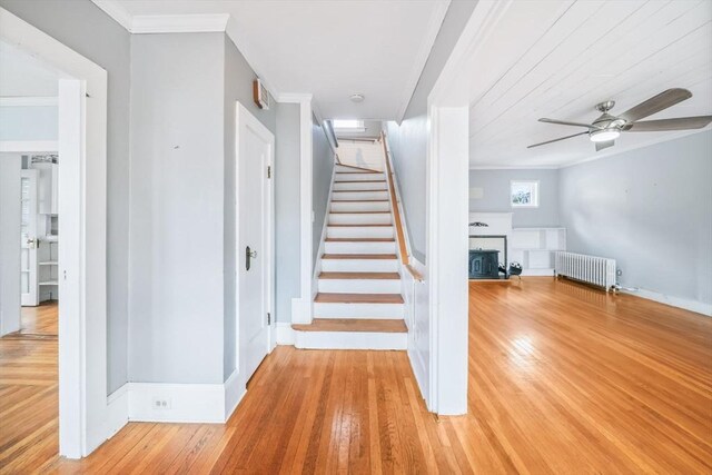 stairway with ceiling fan, radiator, ornamental molding, and wood-type flooring