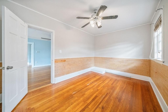 empty room with ceiling fan, wood-type flooring, ornamental molding, and wooden walls