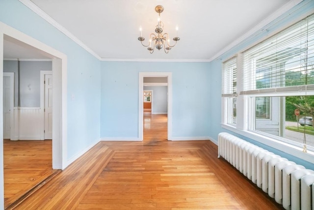 empty room featuring a chandelier, crown molding, radiator heating unit, and light hardwood / wood-style flooring