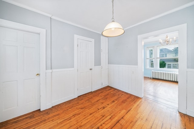 unfurnished dining area featuring radiator heating unit, crown molding, an inviting chandelier, and hardwood / wood-style flooring