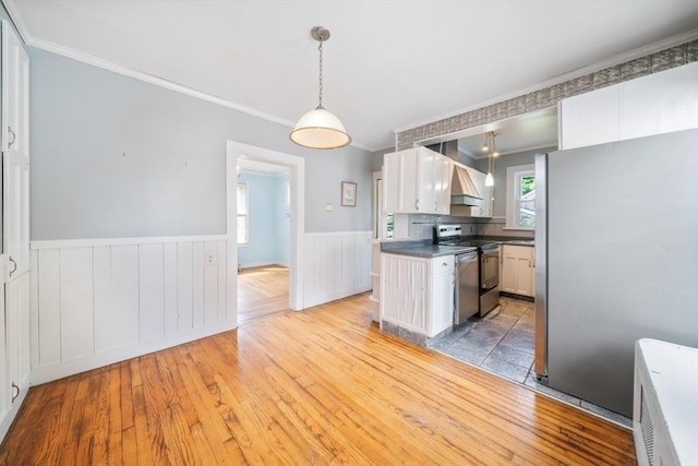 kitchen with decorative light fixtures, crown molding, stainless steel appliances, white cabinets, and hardwood / wood-style flooring