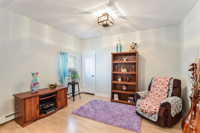 sitting room with a baseboard radiator, a textured ceiling, and light wood-type flooring