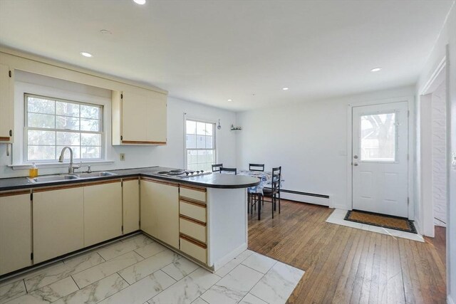 kitchen with baseboard heating, dark countertops, a sink, cream cabinets, and a peninsula