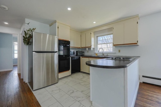 kitchen with a baseboard radiator, dark countertops, a sink, black appliances, and baseboards