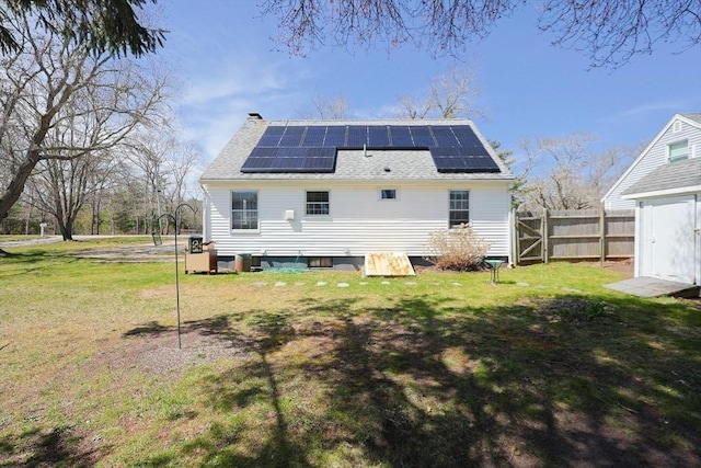 back of house with a chimney, fence, a shingled roof, a yard, and solar panels
