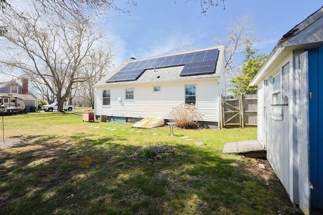back of property with a lawn, roof mounted solar panels, fence, and a shingled roof