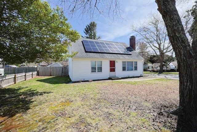 rear view of house featuring a chimney, fence, a shingled roof, a yard, and roof mounted solar panels