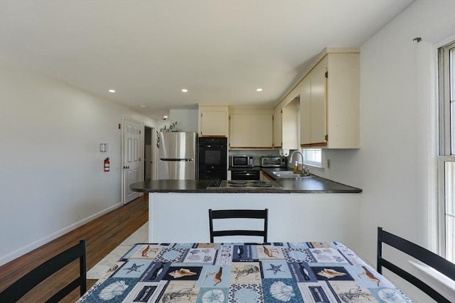 kitchen with dark countertops, wood finished floors, a sink, stainless steel appliances, and a peninsula