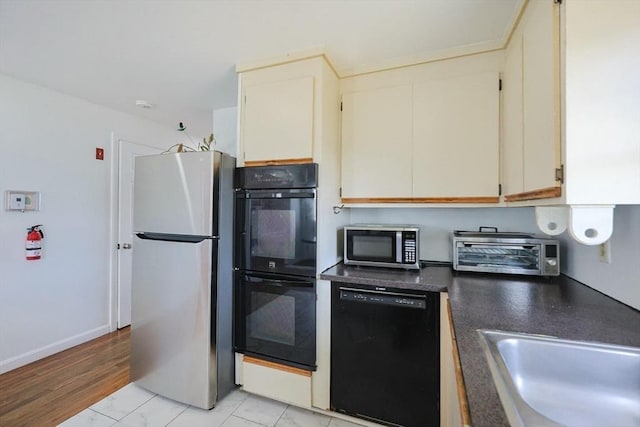 kitchen with a toaster, a sink, dark countertops, black appliances, and cream cabinets