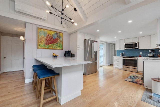 kitchen featuring backsplash, appliances with stainless steel finishes, an inviting chandelier, and light wood finished floors