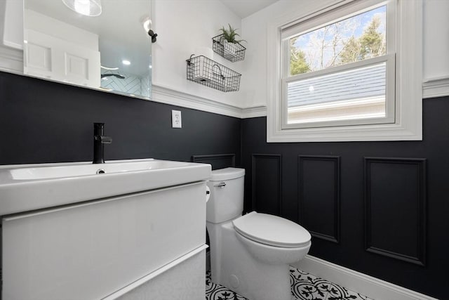 bathroom featuring a decorative wall, toilet, vanity, and walk in shower
