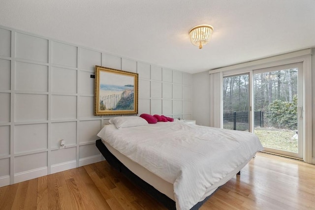 bedroom featuring access to outside, a decorative wall, and wood finished floors