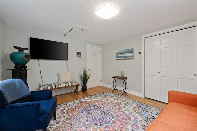 living area featuring light wood-style floors, attic access, baseboards, and a textured ceiling