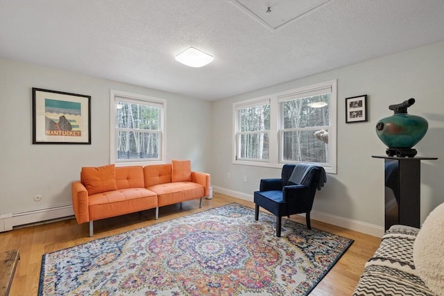 living area with a textured ceiling, wood finished floors, a baseboard heating unit, and baseboards