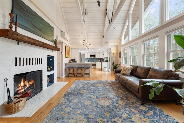 living area with high vaulted ceiling, a brick fireplace, beam ceiling, and light wood-style flooring