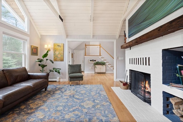 living room with a baseboard heating unit, lofted ceiling with beams, a brick fireplace, and stairway