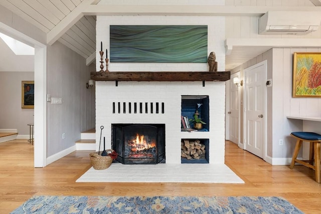 details with baseboards, a wall mounted air conditioner, a brick fireplace, beam ceiling, and wood finished floors