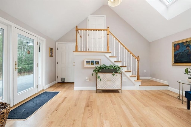 foyer entrance with vaulted ceiling with skylight, baseboards, and wood finished floors