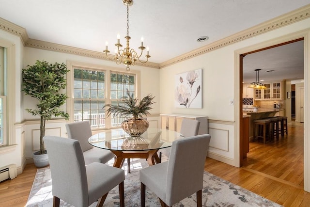 dining area featuring a chandelier, light wood finished floors, a decorative wall, wainscoting, and baseboard heating