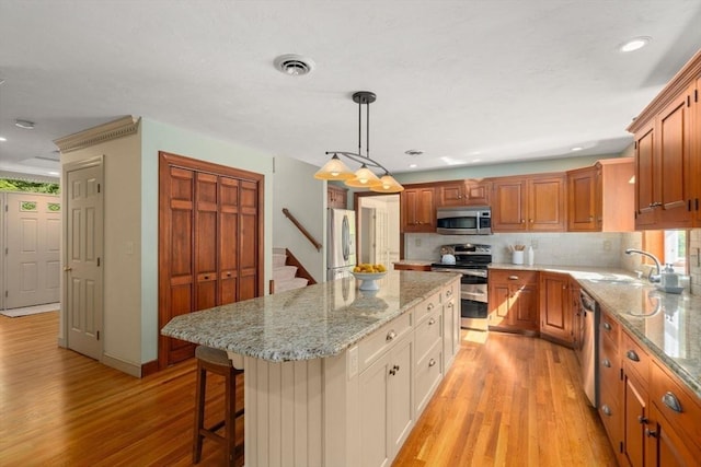 kitchen with appliances with stainless steel finishes, light wood finished floors, a center island, tasteful backsplash, and a breakfast bar