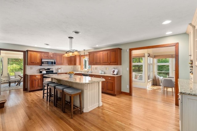 kitchen with appliances with stainless steel finishes, light wood-style floors, brown cabinetry, a kitchen island, and backsplash