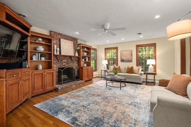 living area featuring a ceiling fan, wood finished floors, a fireplace, a baseboard heating unit, and recessed lighting