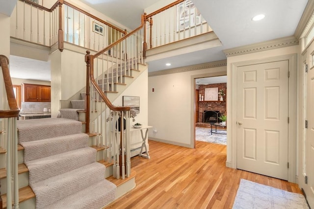 stairs with a high ceiling, wood finished floors, baseboards, a brick fireplace, and recessed lighting