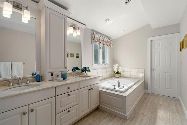 full bathroom with wood finished floors, a bath, double vanity, and lofted ceiling