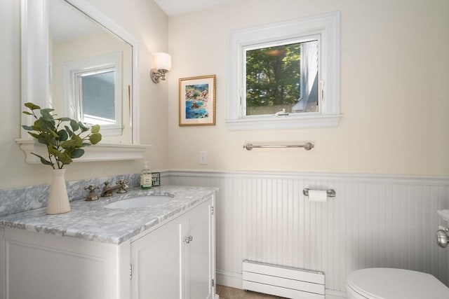 half bathroom with baseboard heating, a wainscoted wall, toilet, and vanity