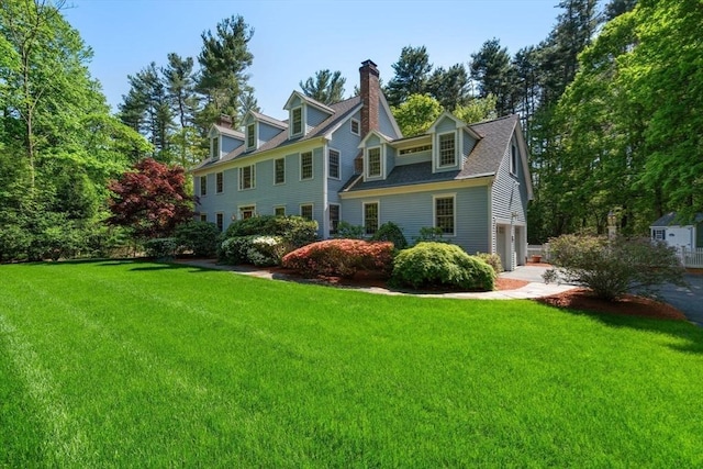 rear view of property with an attached garage, a lawn, driveway, and a chimney