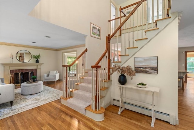 stairway featuring a baseboard radiator, wood finished floors, a high ceiling, and a brick fireplace
