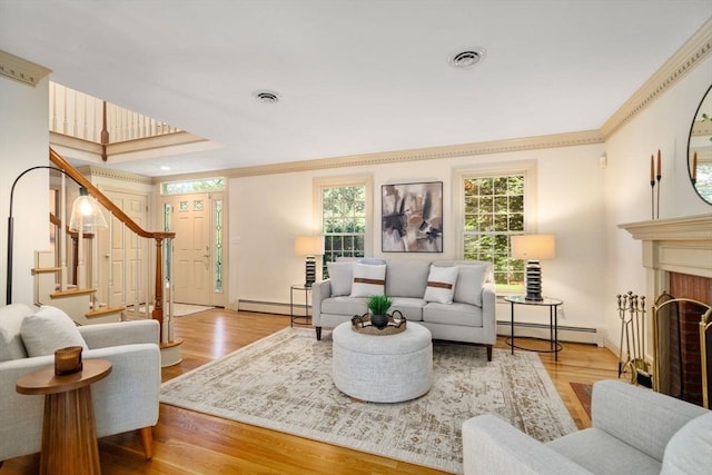 living area featuring baseboard heating, ornamental molding, wood finished floors, stairs, and baseboards