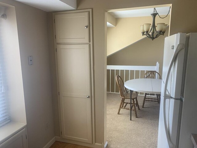 kitchen featuring baseboards, an inviting chandelier, freestanding refrigerator, light countertops, and light colored carpet