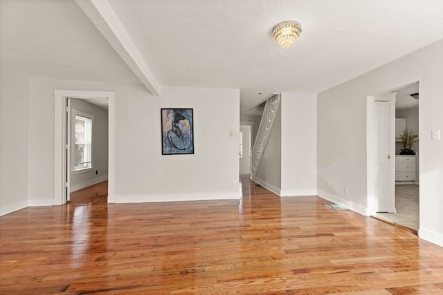 unfurnished room with beamed ceiling and light hardwood / wood-style flooring