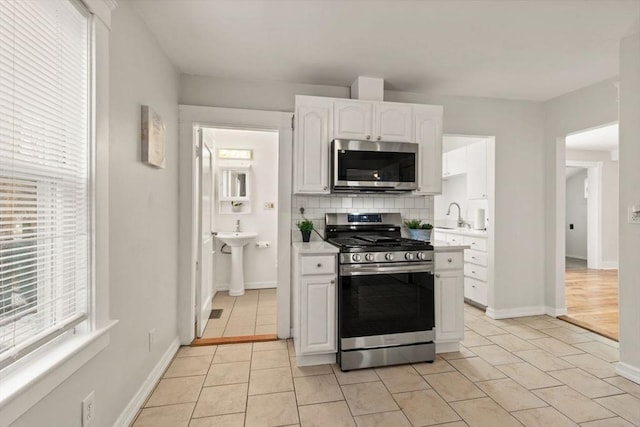 kitchen with light tile patterned floors, white cabinetry, backsplash, stainless steel appliances, and a healthy amount of sunlight