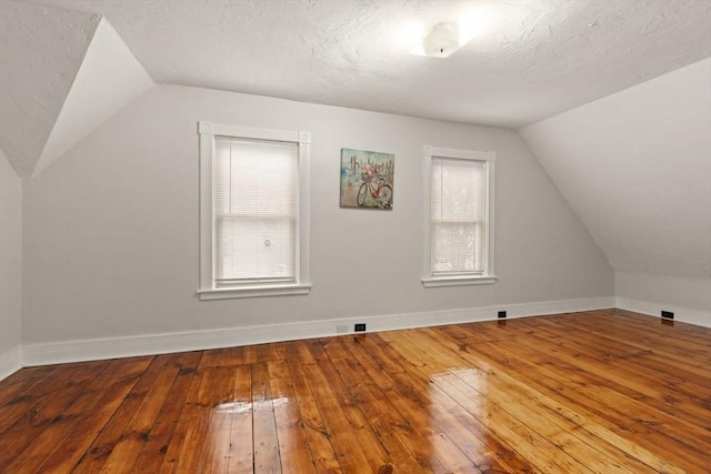 additional living space featuring lofted ceiling, wood-type flooring, and a textured ceiling