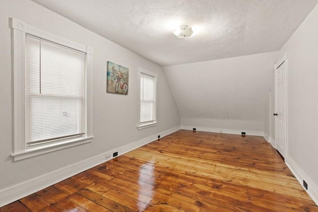 additional living space with wood-type flooring, a textured ceiling, and vaulted ceiling